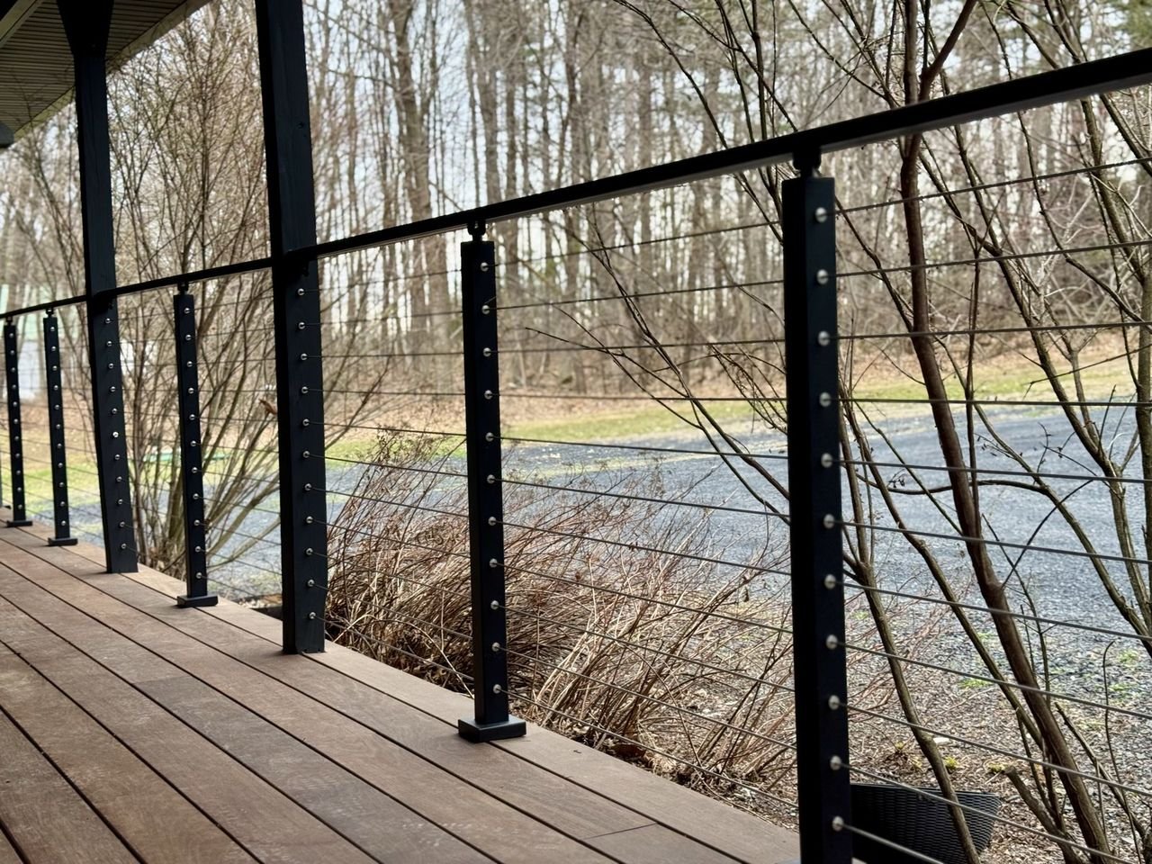Deck with black cable railing looking out through bare trees